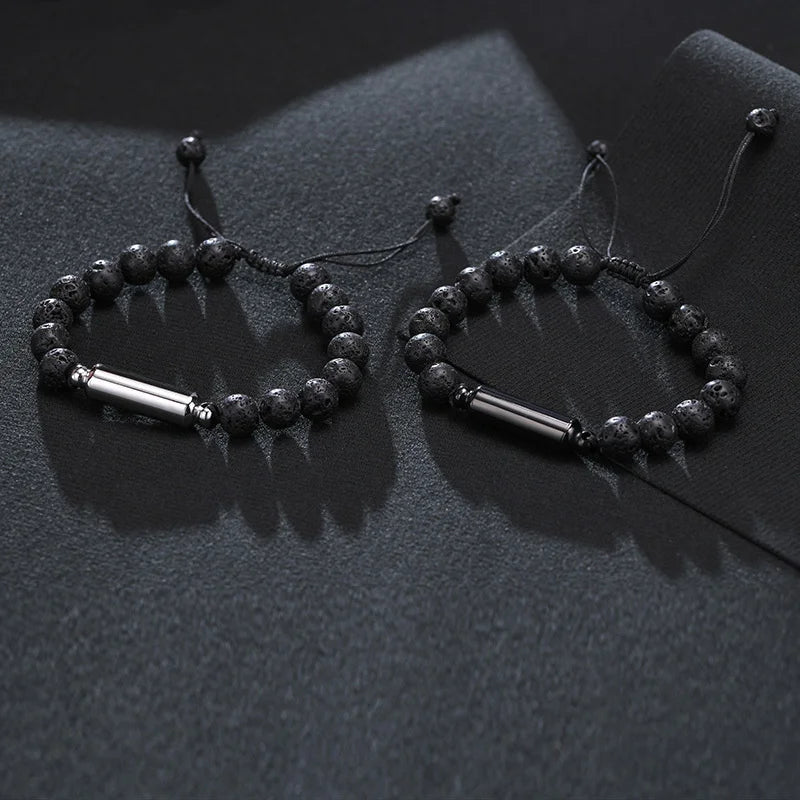 Two black lava stone cremation bracelets with adjustable cords displayed on dark grey fabric