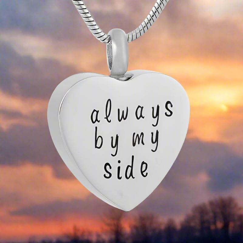 Silver heart-shaped cremation urn pendant engraved with "Always by My Side" on a chain, front view