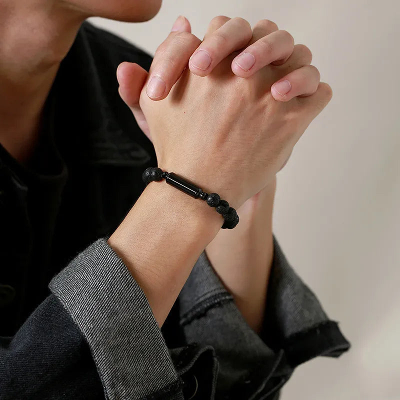 Black lava stone cremation bracelet worn on a man's wrist with hands clasped