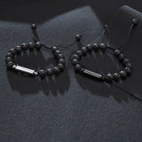 Two black lava stone cremation bracelets with adjustable cords displayed on dark grey fabric
