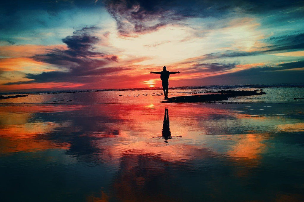 Silhouette of a person with their arms open on the beach with a beautiful sunset behind them 