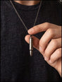 Man holding the rifle bullet cremation necklace pendant on its chain, worn over a dark shirt