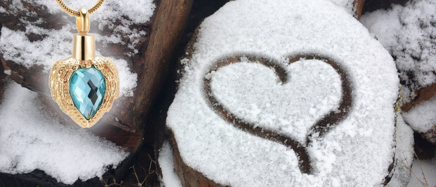 Picture of a heart drawn in some snow on top of some wood includes a silhouette of an urn necklace